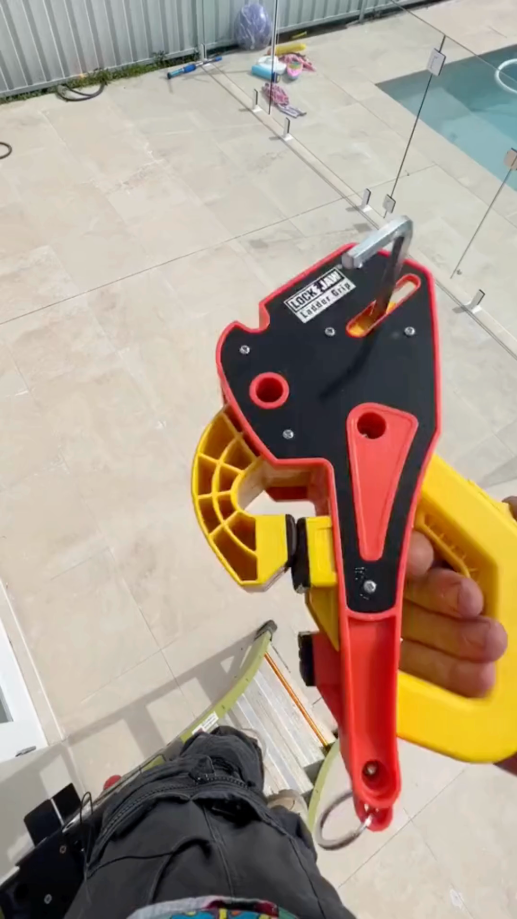 Person holding a Lock Jaw Ladder Grip, a safety tool for stabilizing ladders, with a poolside background.