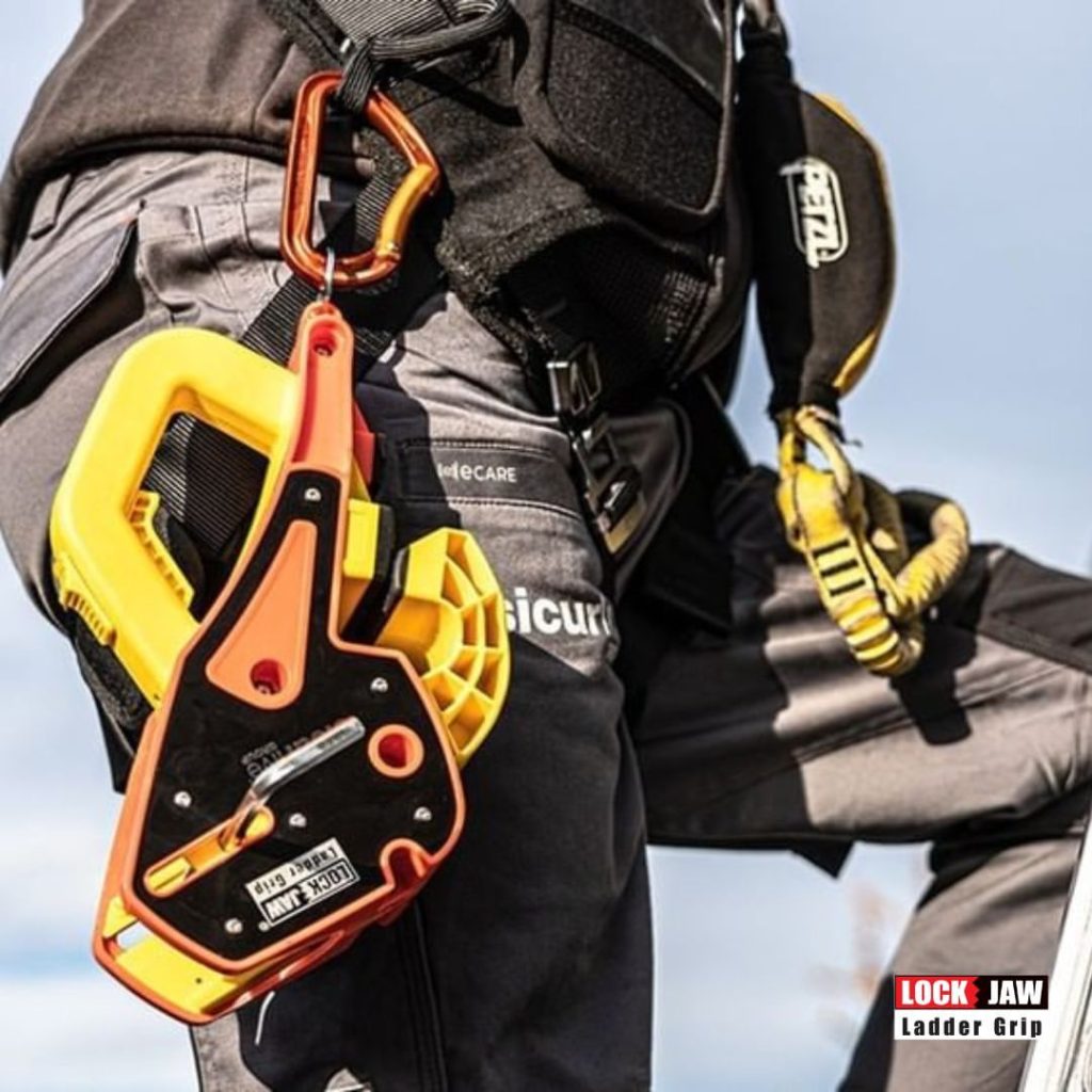 A person wearing a yellow Petzl helmet and safety harness holds a Lock Jaw Ladder Grip.