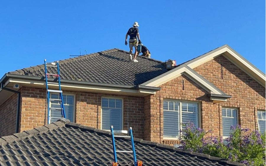 Electricians working on a residential roof above two extension ladders