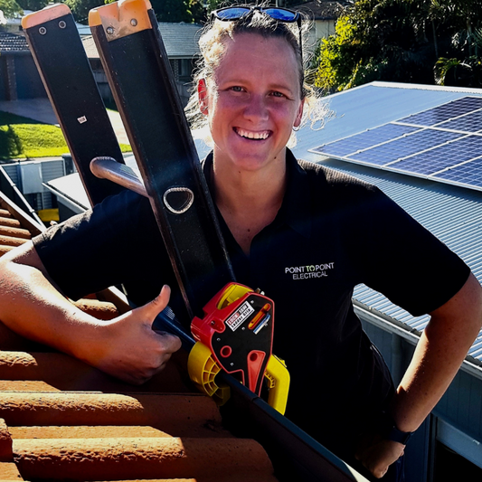 Electrician smiling while using Lock Jaw Ladder Grip for safe roof access on a sunny day with solar panels in the background.