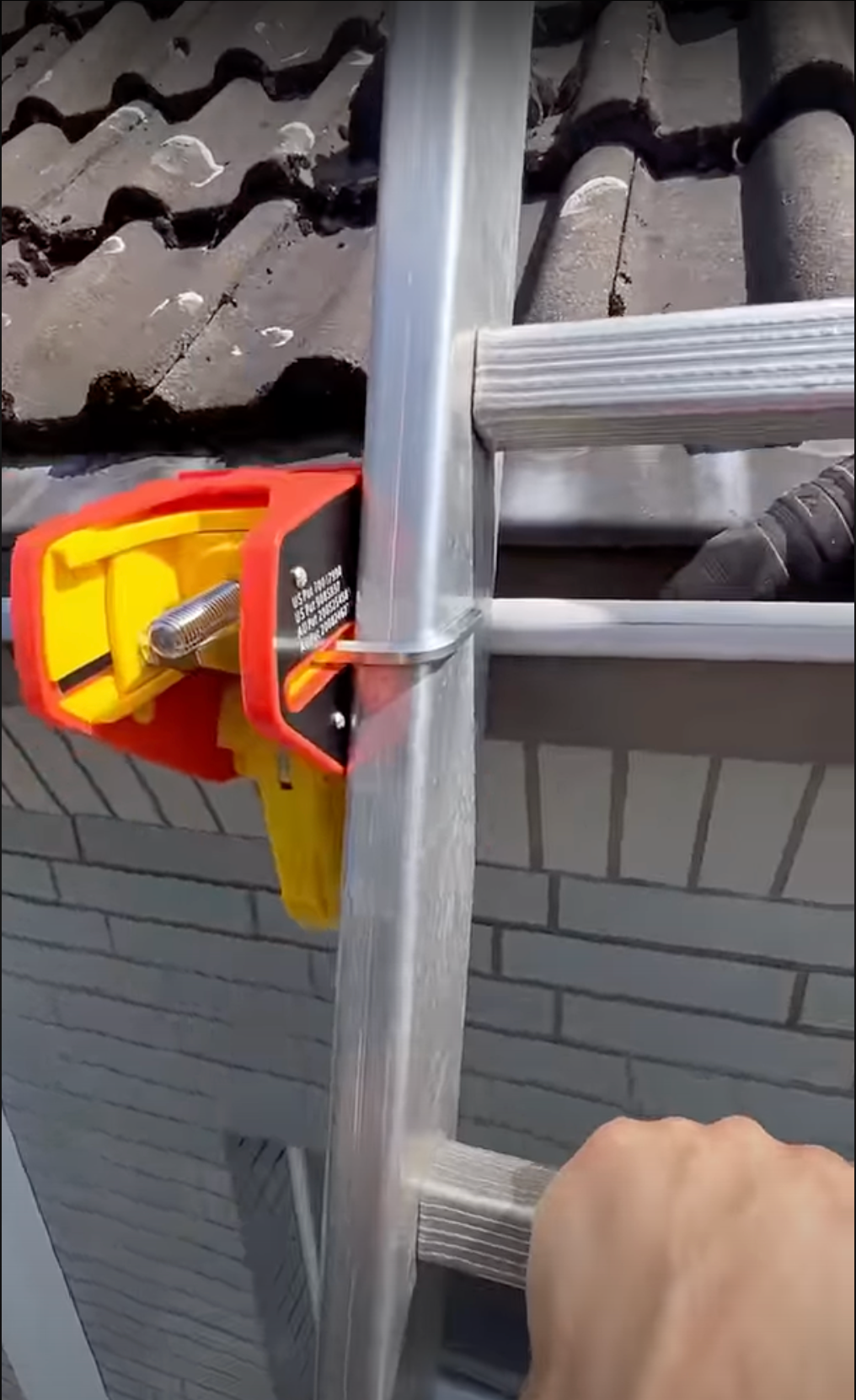 Close-up of a Lock Jaw Ladder Grip securing a ladder to a gutter on a house with a tiled roof.