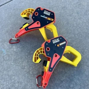 Two Lock Jaw Ladder Grips, safety devices in red, black, and yellow, rest on a concrete surface.