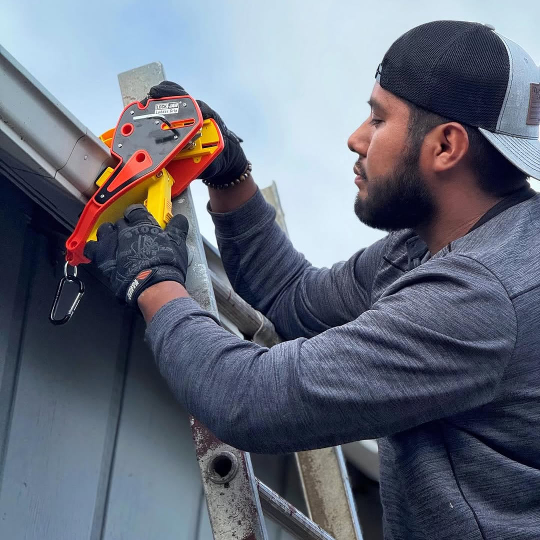 Roofer clamping a Lock Jaw Ladder Grip onto the gutter by hand