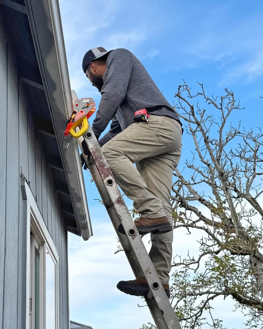 Roofer climbing an extension ladder locked to the gutter with a Lock Jaw Ladder Grip