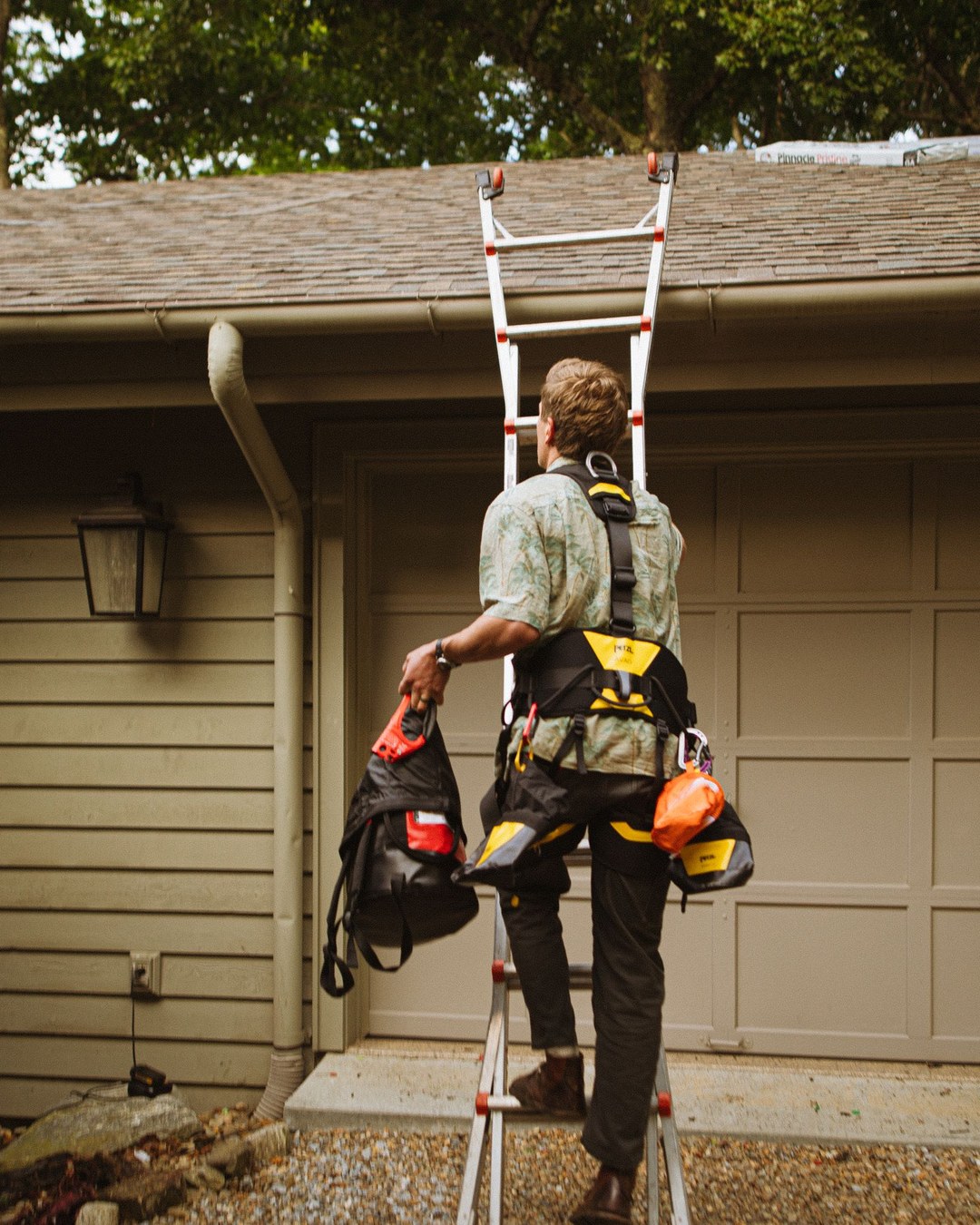 Electrician climbing an extension ladder resting on the gutter of a house