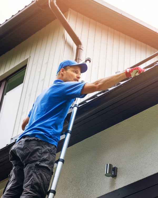 Gutter cleaner on a ladder clearing debris from a house gutter