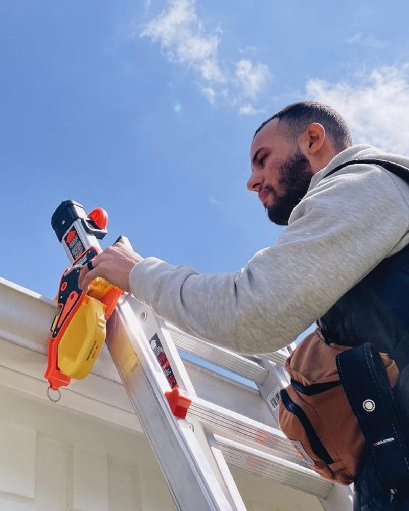 An electrician holding a Lock Jaw Ladder Grip beside an extension ladder